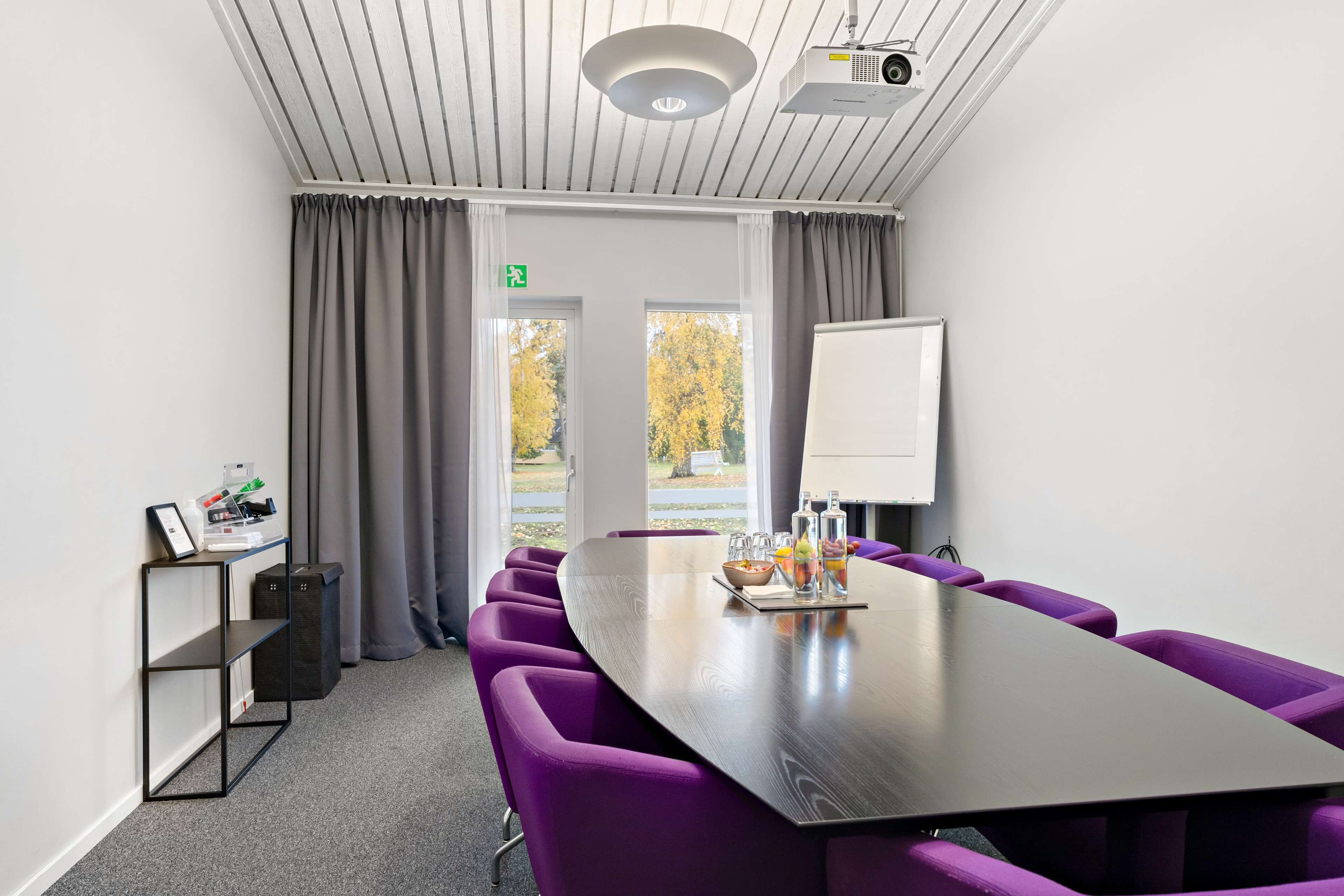 Ett konferensrum med ett långt bord, lila stolar, en whiteboard och en projektor.