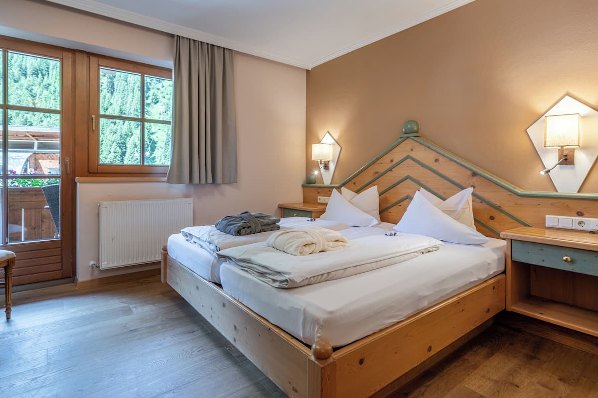 A wooden bed in a room with a window, two bedside tables, and a wall-mounted lamp.