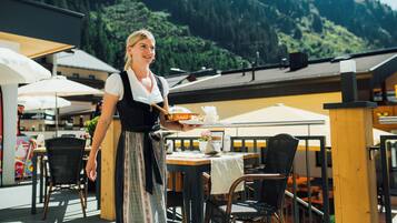 A restaurant with outdoor seating, a waitress serving food, and a mountainous backdrop.