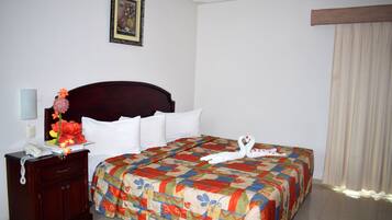 A hotel room with a wooden headboard, a floral arrangement on the nightstand, a colorful bedspread, and a framed picture on the wall.