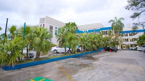 A parking lot with several cars, palm trees, and a building with a blue and white facade. - Hotel Principe (Chetumal)
