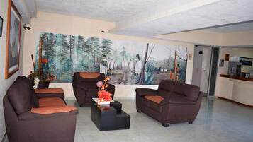 Un salón amplio con dos sofás marrones, una mesa de centro negra y un gran mural con motivos forestales en la pared.