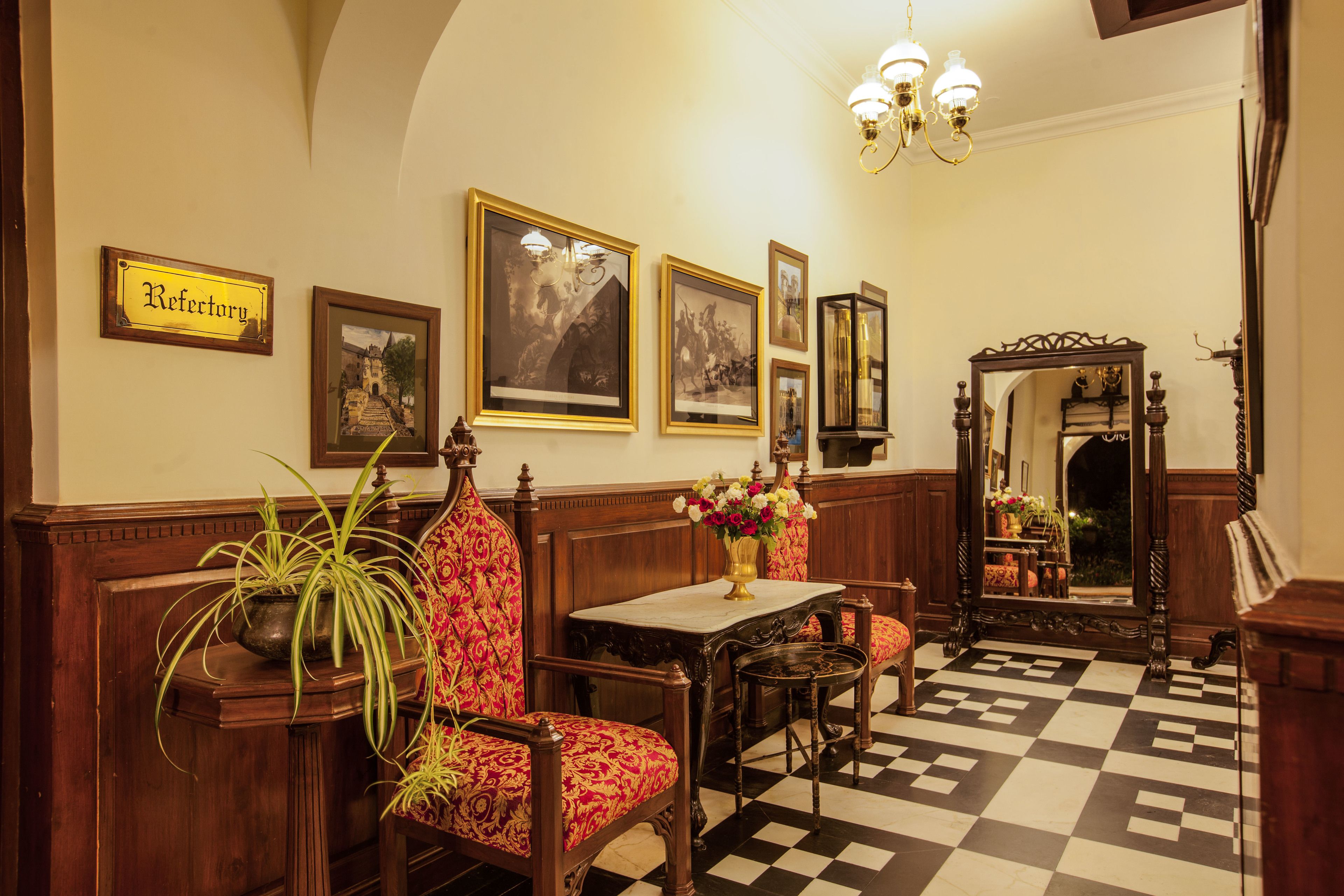 A room with a checkered floor, a wooden bench, a table with a vase of flowers, and framed pictures on the wall.