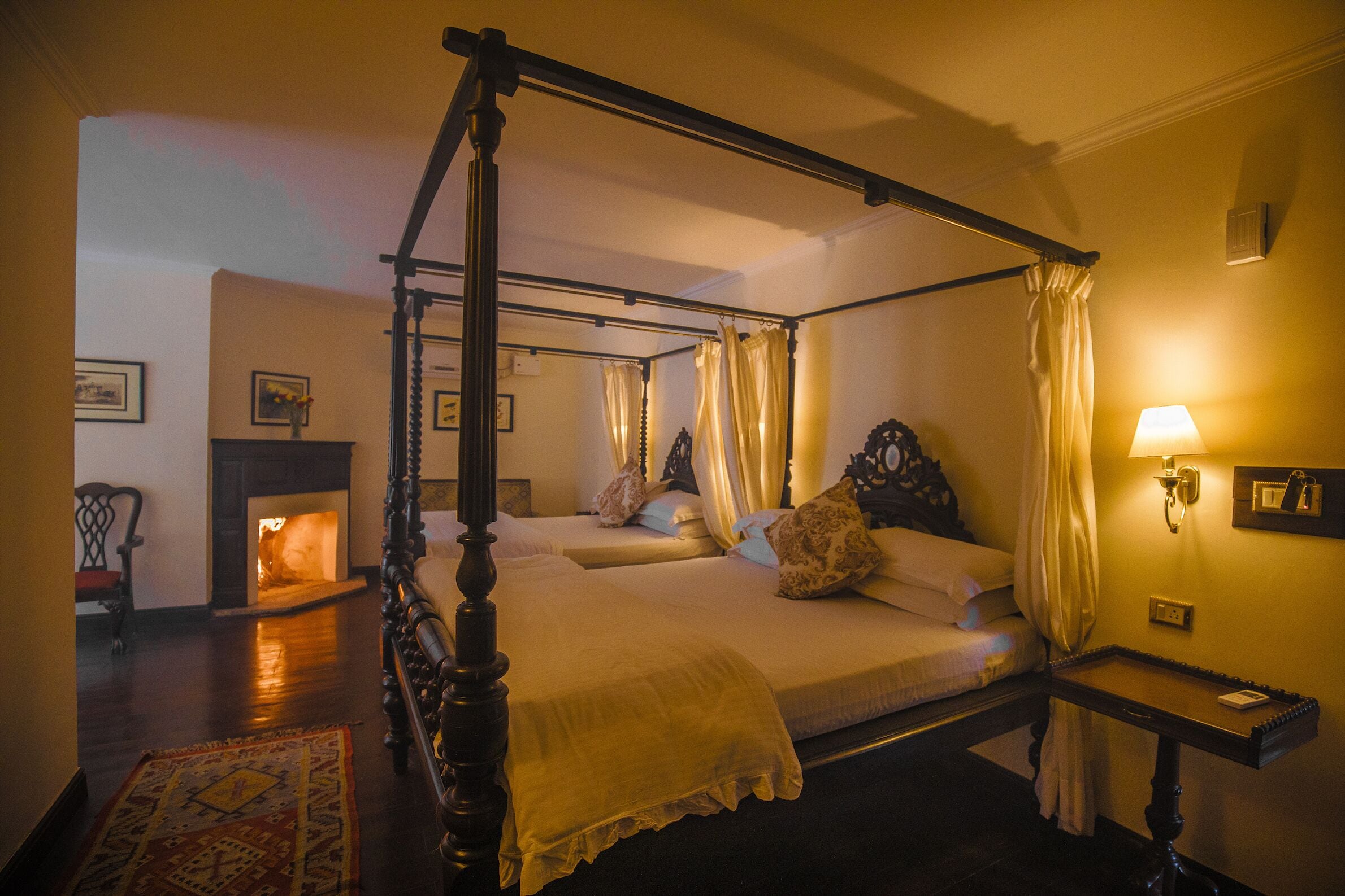A four-poster bed with a canopy, a bedside table with a lamp, and a fireplace in the background.