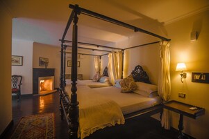 Una cama con dosel, una mesita de noche con lámpara y una chimenea al fondo.