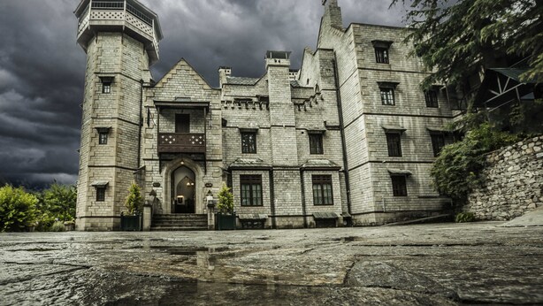 A large, historic stone building with multiple towers and a central entrance.