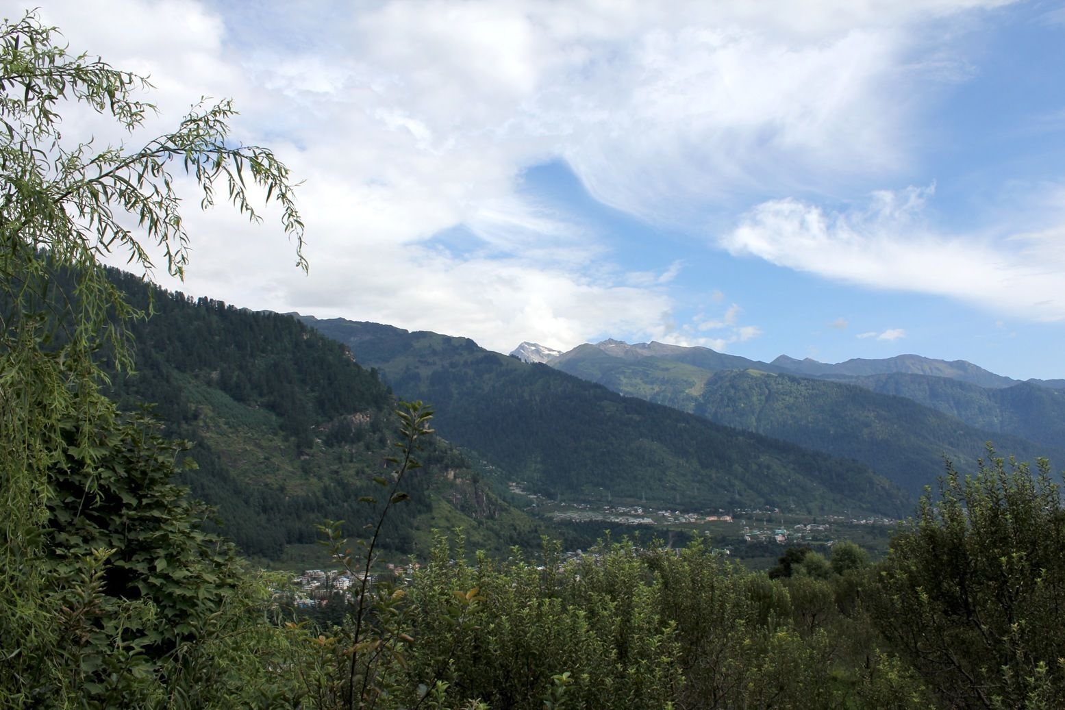 A mountainous landscape with dense forests and a valley with buildings.