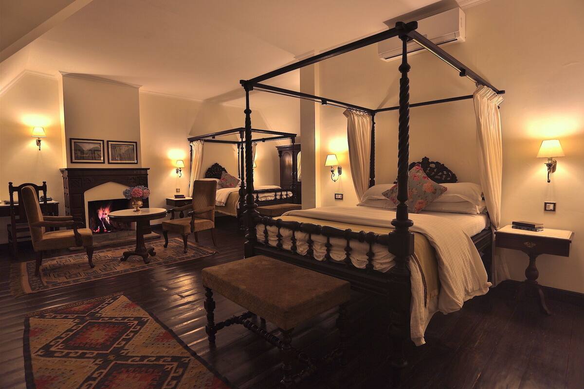 A four-poster bed with a canopy, a round table, a bench, and a fireplace.
