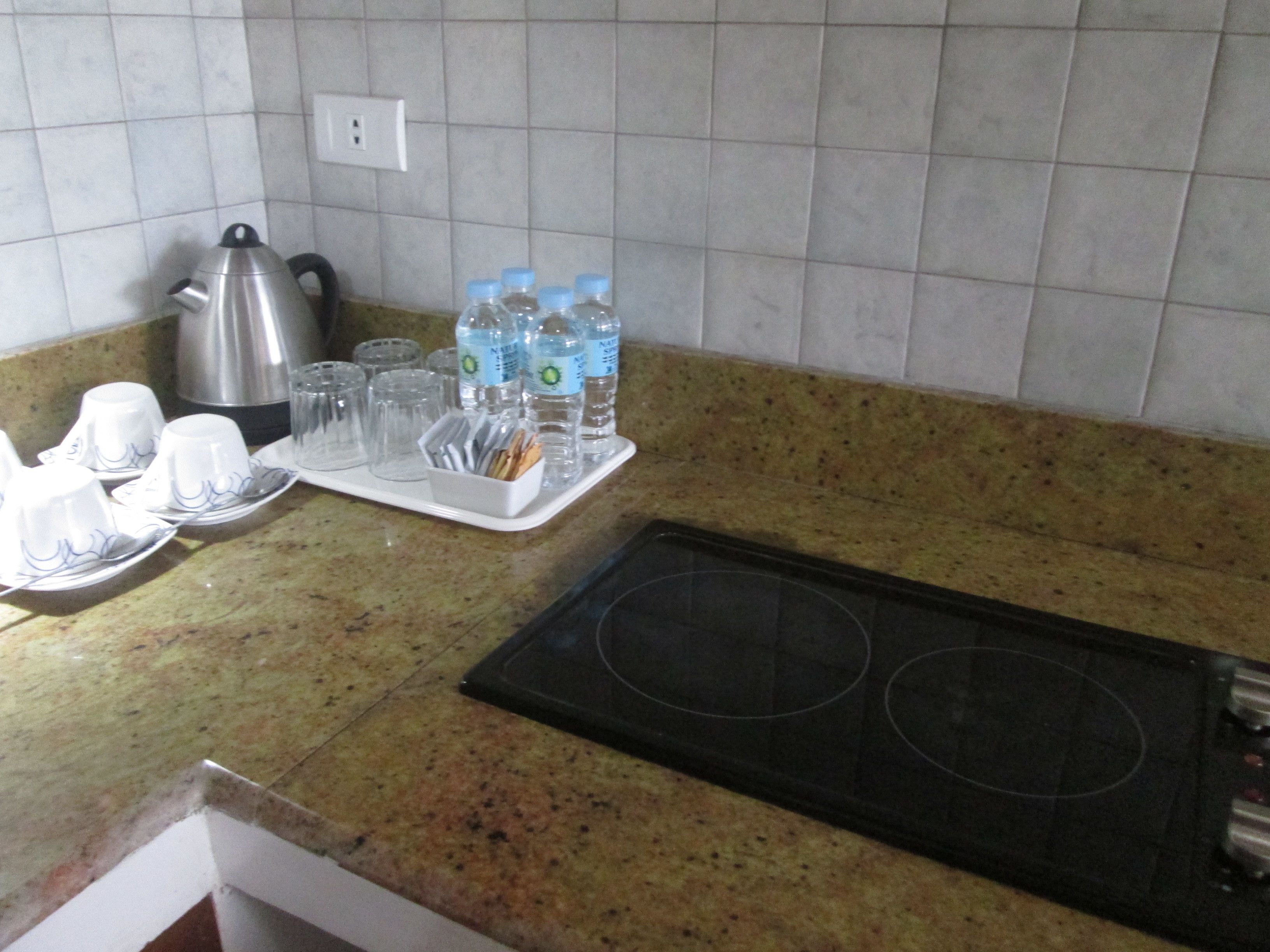 Una cocina con encimera de granito, hervidor, tostadora y una bandeja con tazas y botellas de agua.