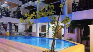 Piscina com degraus de acesso, rodeada por um edifício com vários níveis e varandas.