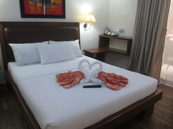 A hotel room with a neatly made bed, a wall-mounted lamp, a small table with a kettle, and a painting above the bed. - Giulius Boracay Italian Resort (Boracay Island)