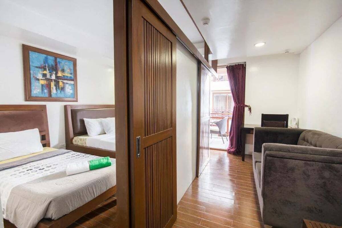 Une chambre d’hôtel avec deux lits, un canapé, une porte en bois et un tableau au mur.