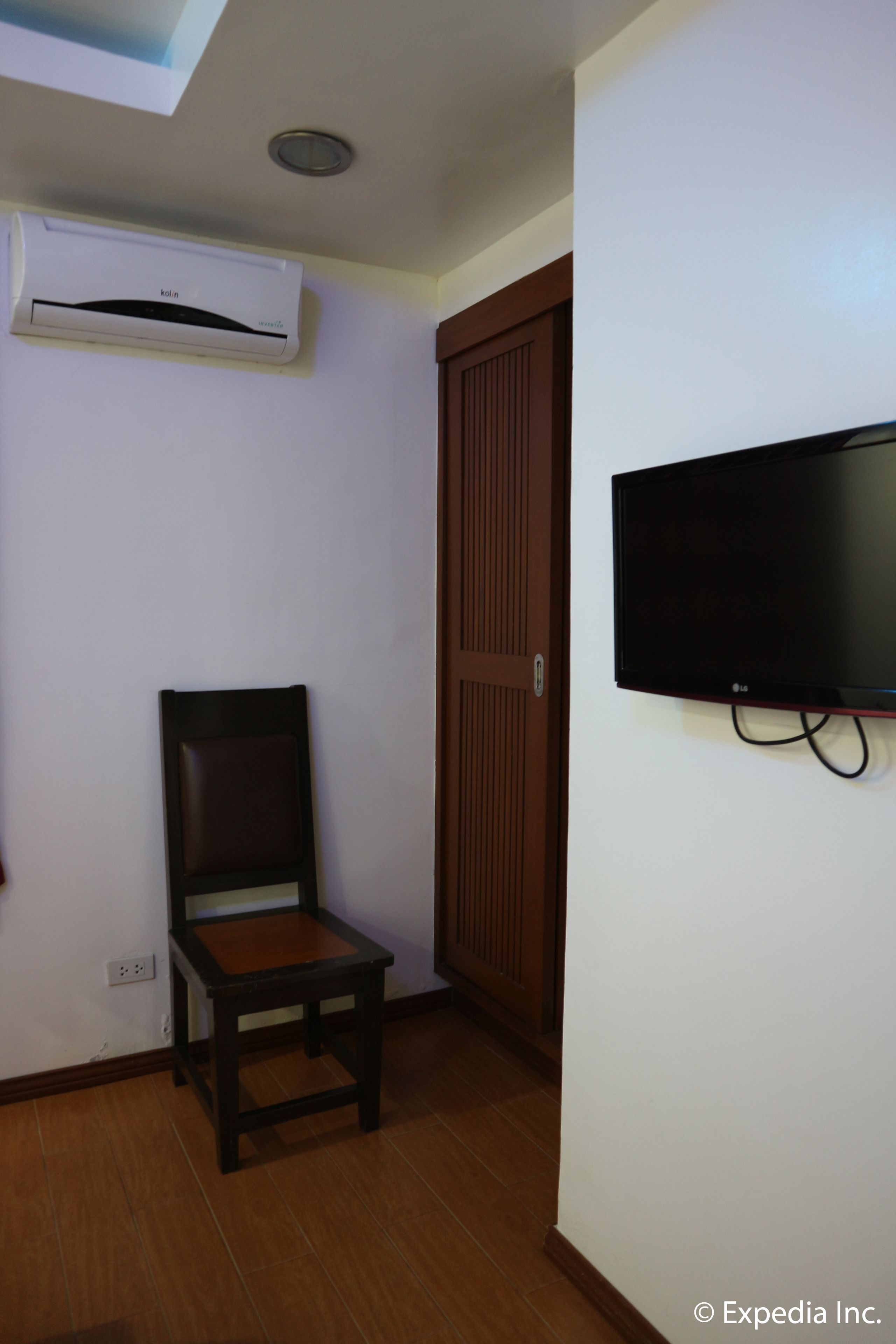 A room with a wooden chair, a television mounted on the wall, and an air conditioning unit on the ceiling.