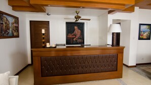 Uma mesa de recepção com encosto de couro texturizado, um ventilador de teto e obras de arte emolduradas nas paredes.