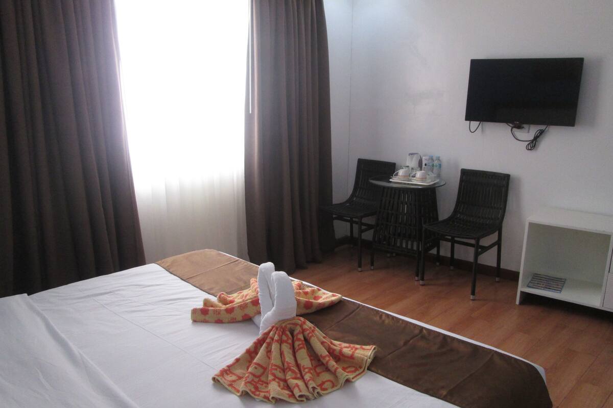 Une chambre d’hôtel avec un lit, un téléviseur fixé au mur, une petite table avec des chaises et un radiateur.