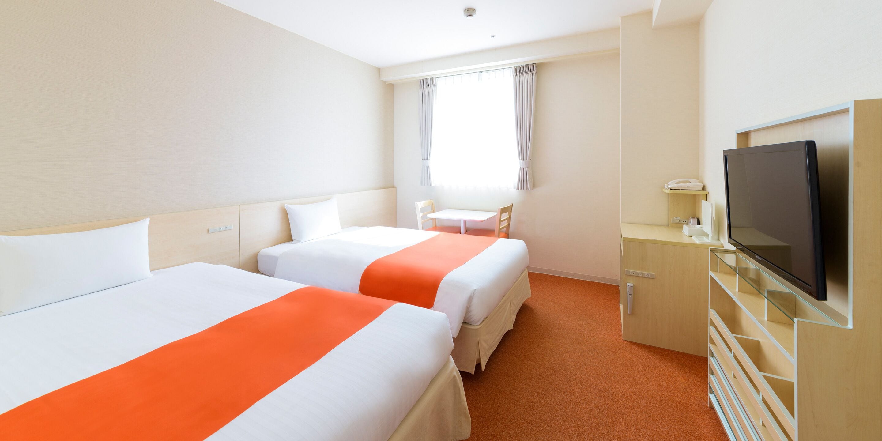 A hotel room with two beds, a television, a desk, and a window with curtains.