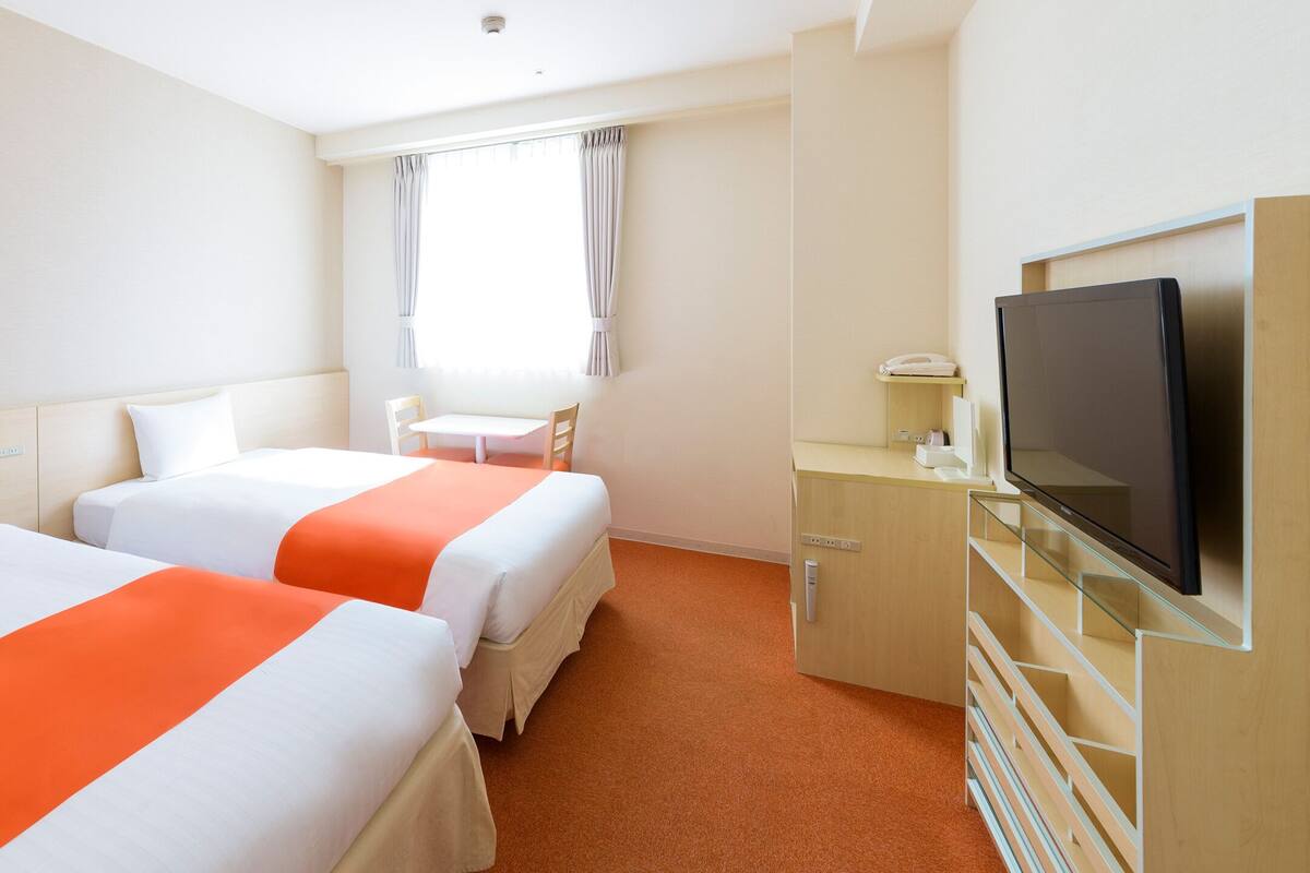 Una habitación de hotel con dos camas, televisión, escritorio y ventana con cortinas.