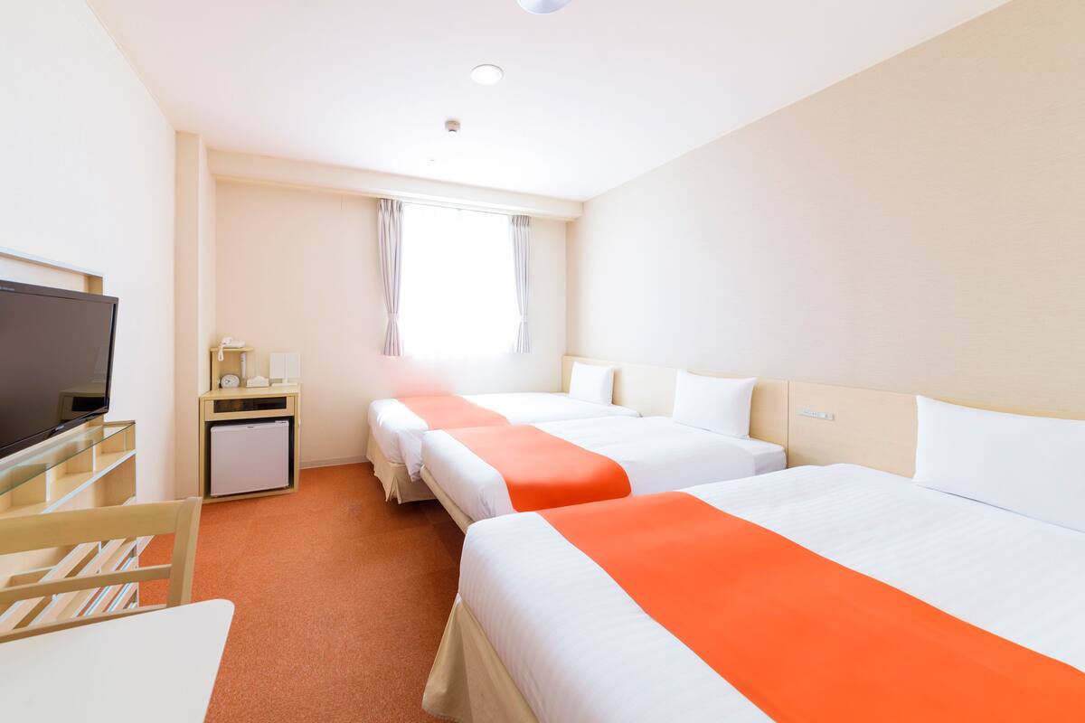 Habitación de hotel con dos camas, televisor, escritorio y ventana con cortinas.