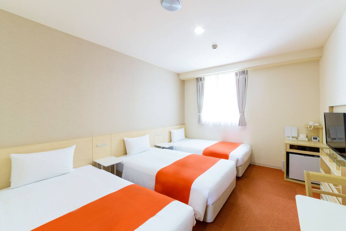 Habitación de hotel con tres camas individuales, un escritorio, una silla, un televisor y un minibar.