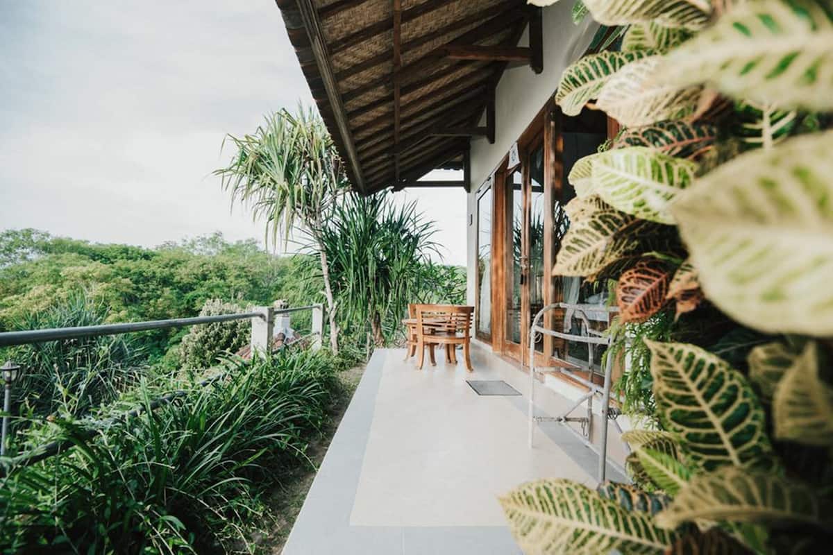 A covered outdoor seating area with a view of lush greenery and a wooden table and chairs.