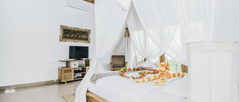 A bedroom with a bed under a canopy, a television on a wooden stand, and a framed picture on the wall.