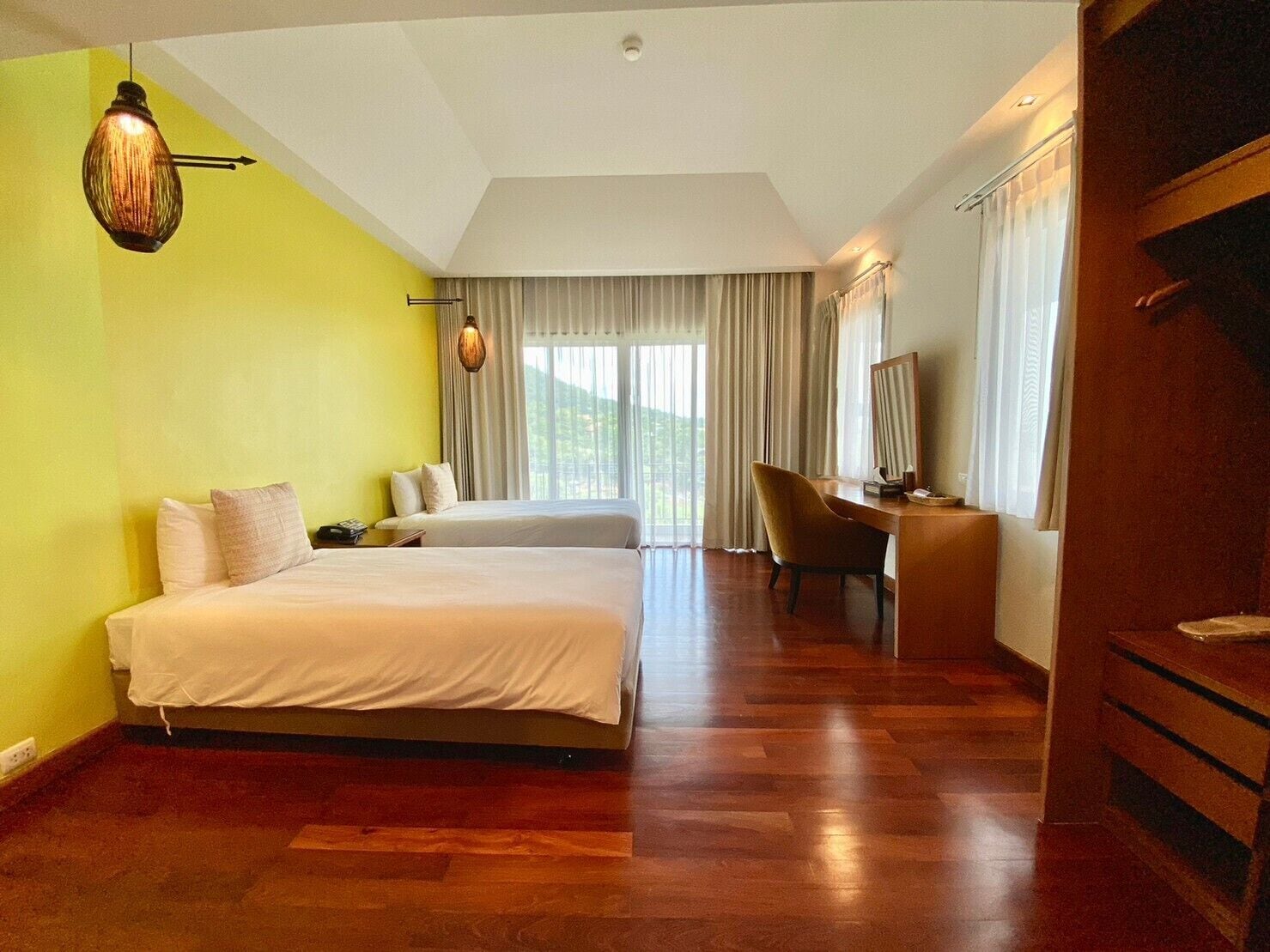 Habitación de hotel con dos camas, un escritorio, una silla y un ventanal con cortinas.