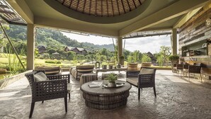 Eine Lounge im Freien mit Korbmöbeln, einem runden Tisch und Blick auf eine üppige Landschaft.