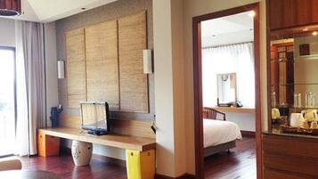 A hotel room with a wooden floor, a bed, a desk with a chair, a large mirror, and a wardrobe.