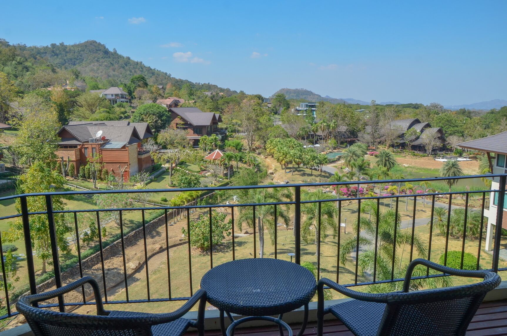 A balcony with wicker furniture and a view of a residential area with houses and greenery.