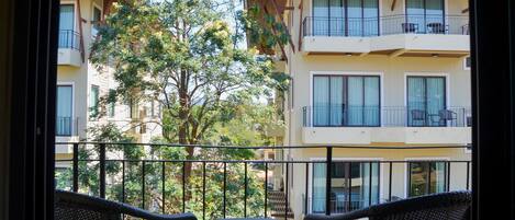 A balcony with wicker furniture, a glass table, and a view of a multi-story building with balconies and windows.