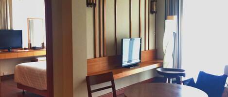 A hotel room with a bed, a TV, a wooden table, and a chair.