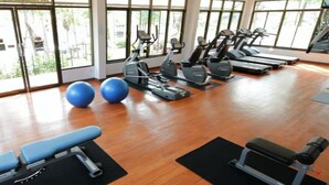 Ein Fitnessraum mit Trainingsgeräten, großen Fenstern und Holzboden.