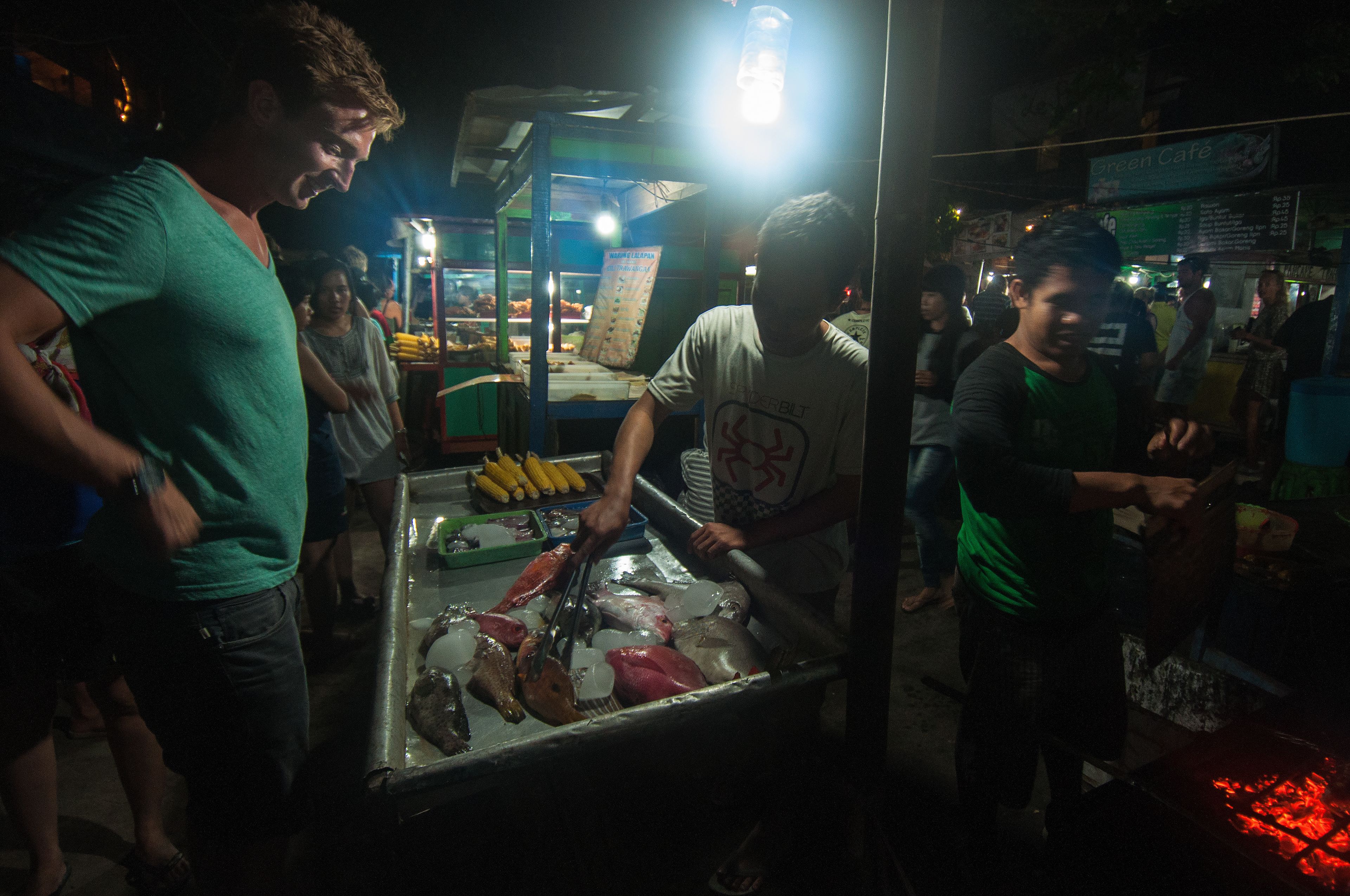 A busy street food stall with a cart filled with various meats and a grill in the background.
