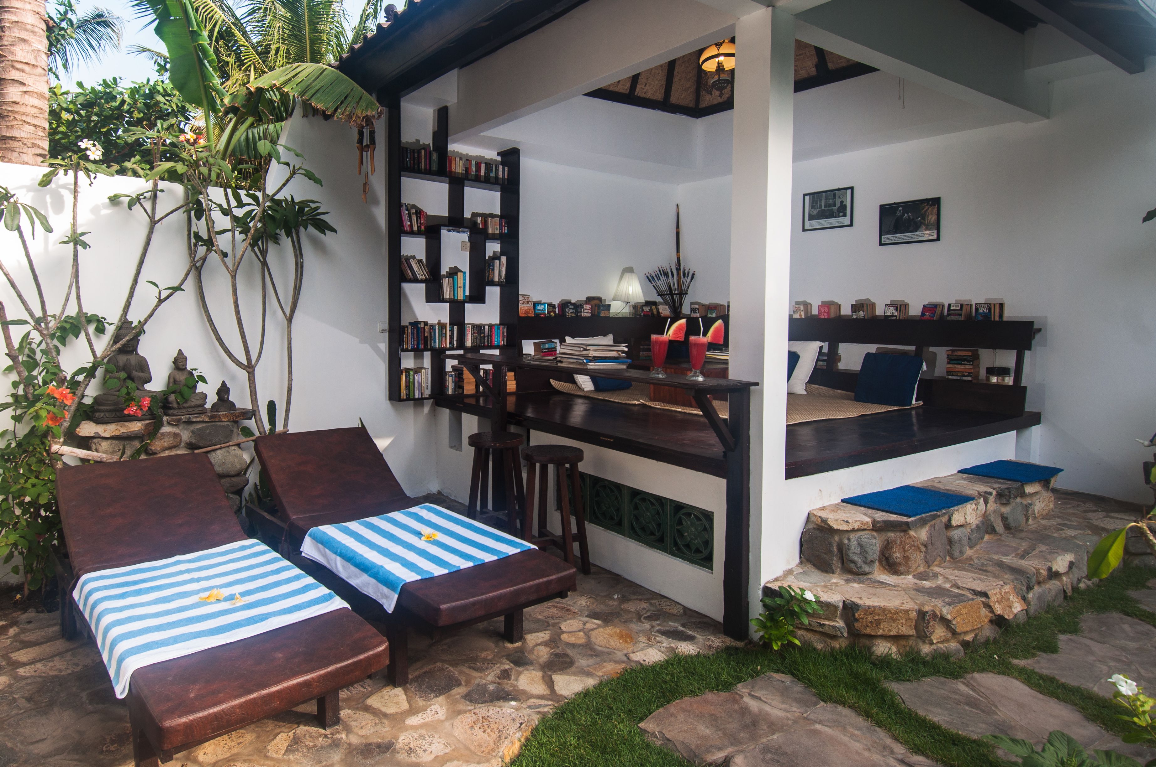 Eine private Außenlounge mit zwei Liegestühlen, einer stentetuierten Terrasse, einer kleinen Bar mit Hockern und einem Bücherregal voller Bücher.