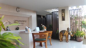 Un espace d’accueil comprenant un bureau en bois, deux chaises en bois, une horloge et une statue d’éléphant décorative.