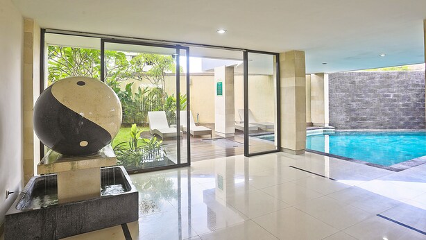 Un espace piscine intérieur moderne, doté d’une paroi en verre, de chaises longues et d’une grande sphère décorative.