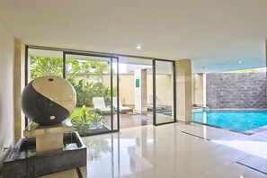 A modern indoor pool area with a glass partition, lounge chairs, and a large decorative sphere. - Anumana Bay View (Jimbaran)