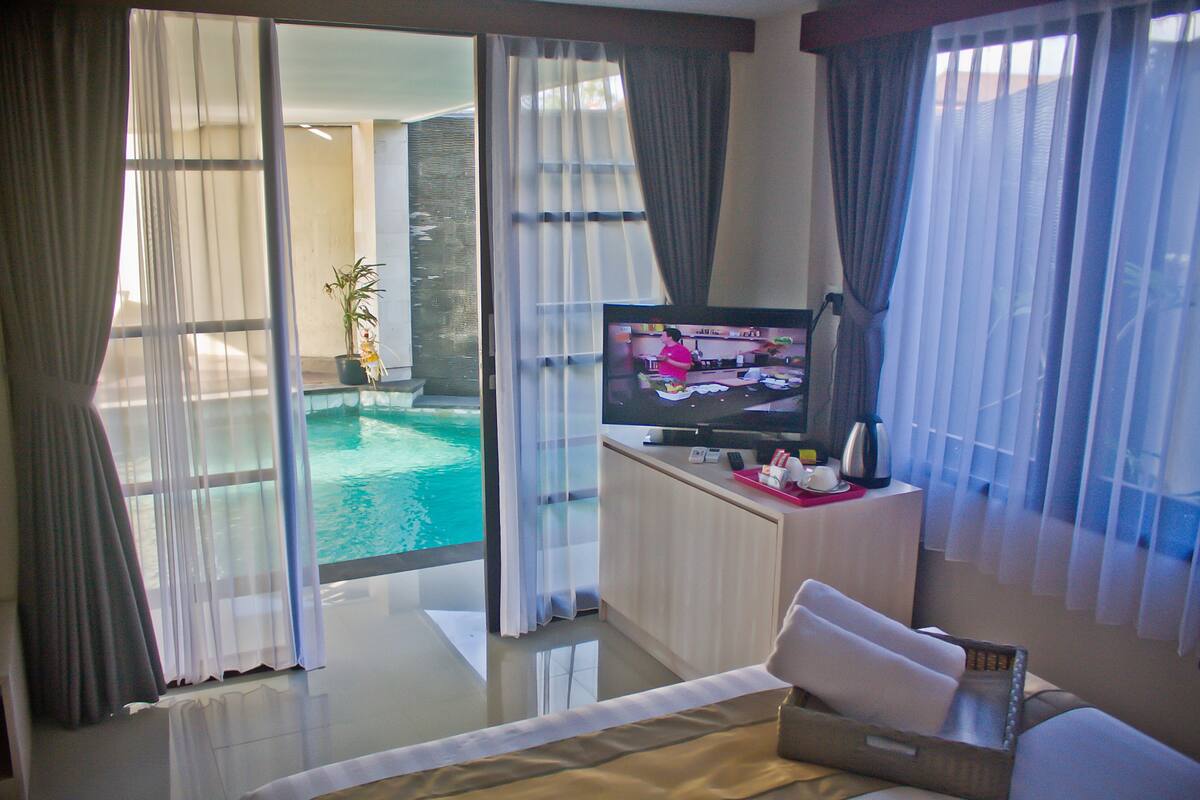 A hotel room with a large window, a flat-screen TV, a bed, and a small table with a remote control.