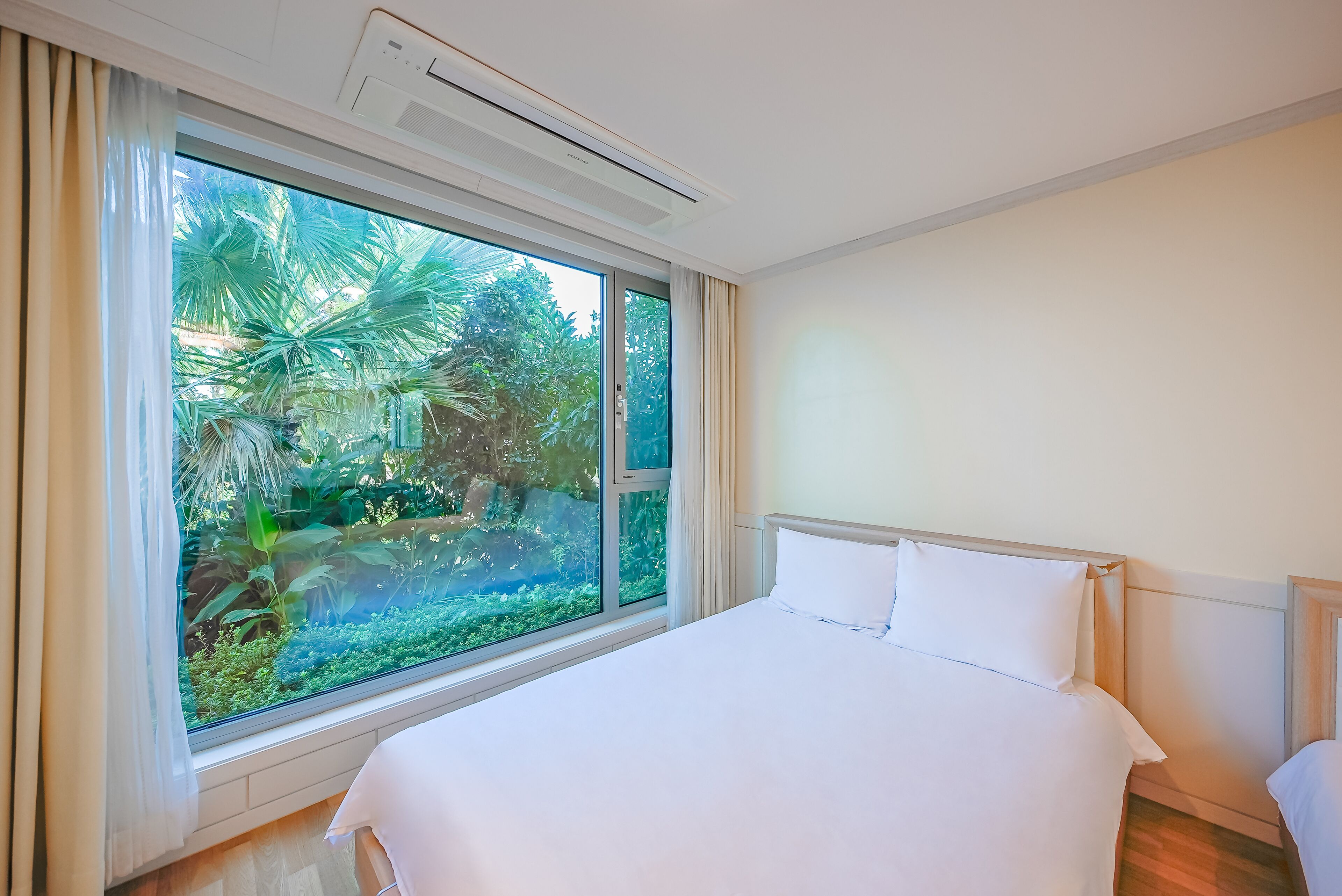 A hotel room with a large window, a bed, and a ceiling air conditioner.