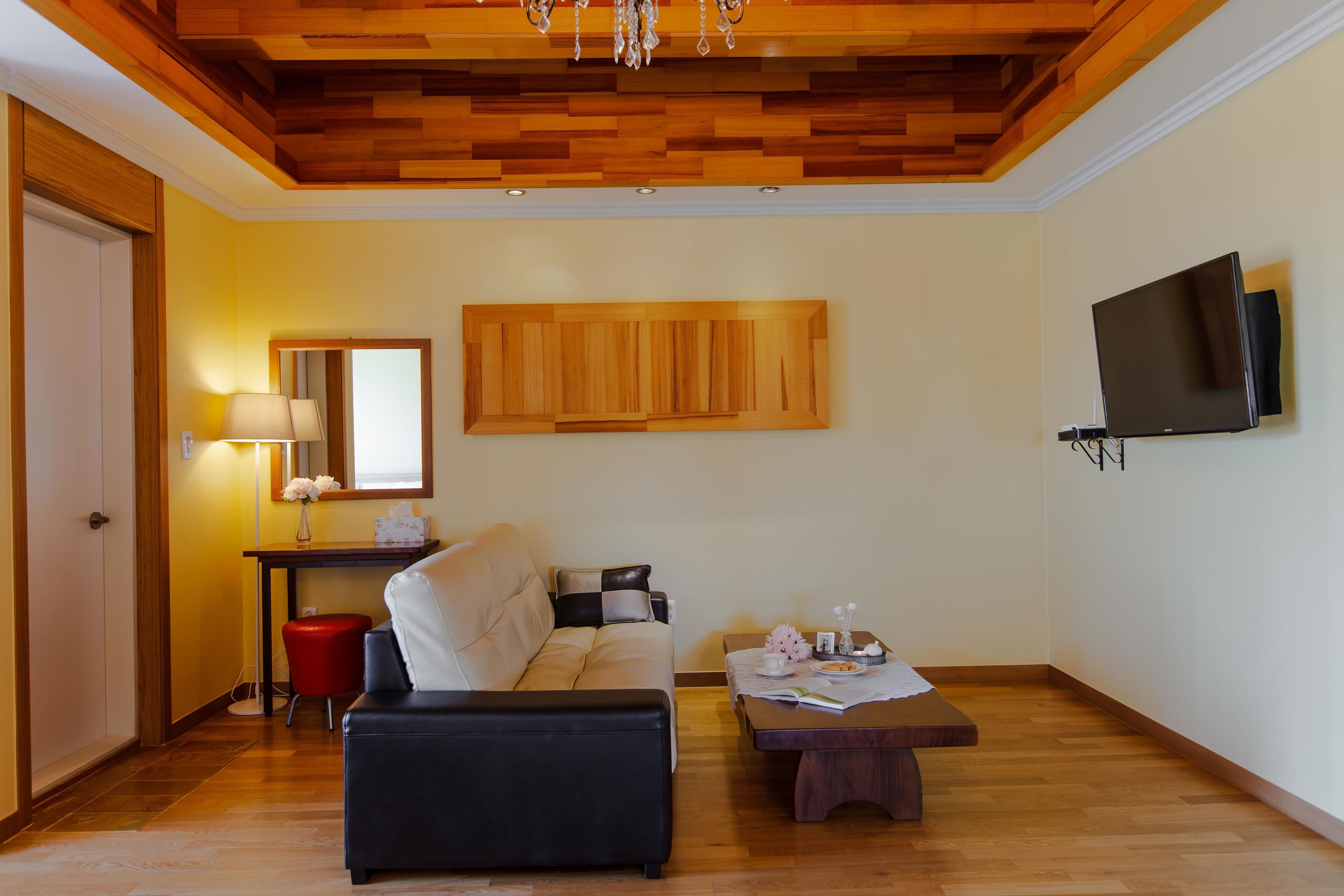A living room with a sofa, a coffee table, a TV mounted on the wall, and a wooden ceiling.