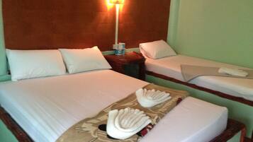 Habitación de hotel con dos camas, cada una con ropa de cama y almohadas blancas. Se observa un mesita de noche con una lámpara y una pequeña mesa con una caja de pañuelos y una botella.