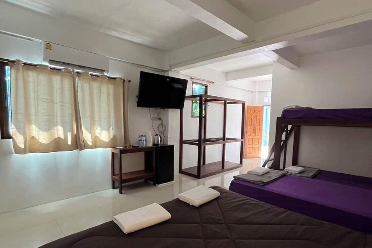 Quarto com uma cama grande, uma escrivaninha com computador, uma televisão e uma beliche.
