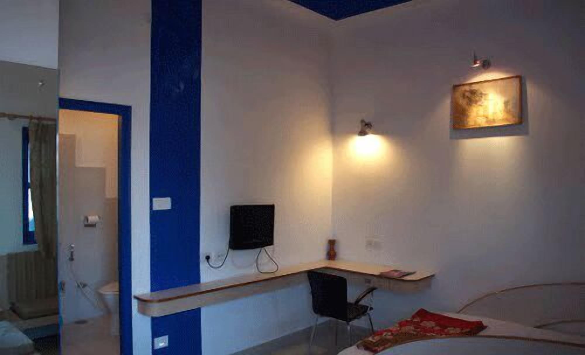 A bedroom with a bed, a desk, a chair, a TV, and a wall-mounted light.