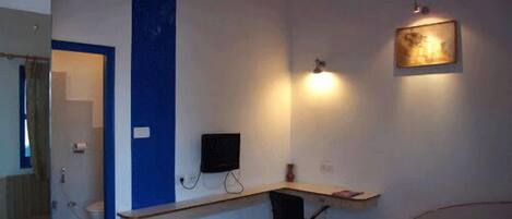 A bedroom with a bed, a desk, a chair, a TV, and a wall-mounted light.