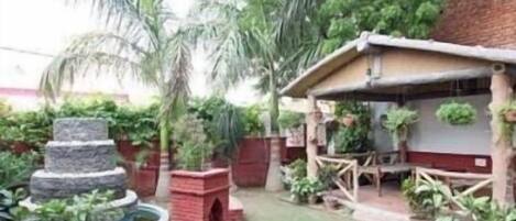A garden with a stone fountain, a small brick structure, and various potted plants.