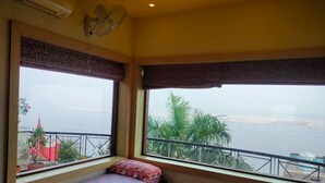 Une chambre avec un lit, une fenêtre donnant sur la mer et un balcon agrémenté de plantes.