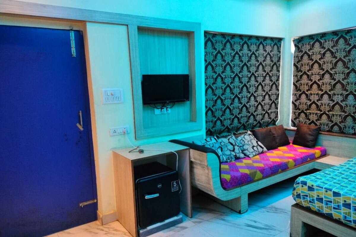 A compact room with a blue door, a small desk with a computer, a bed with a colorful quilt, and patterned wallpaper.