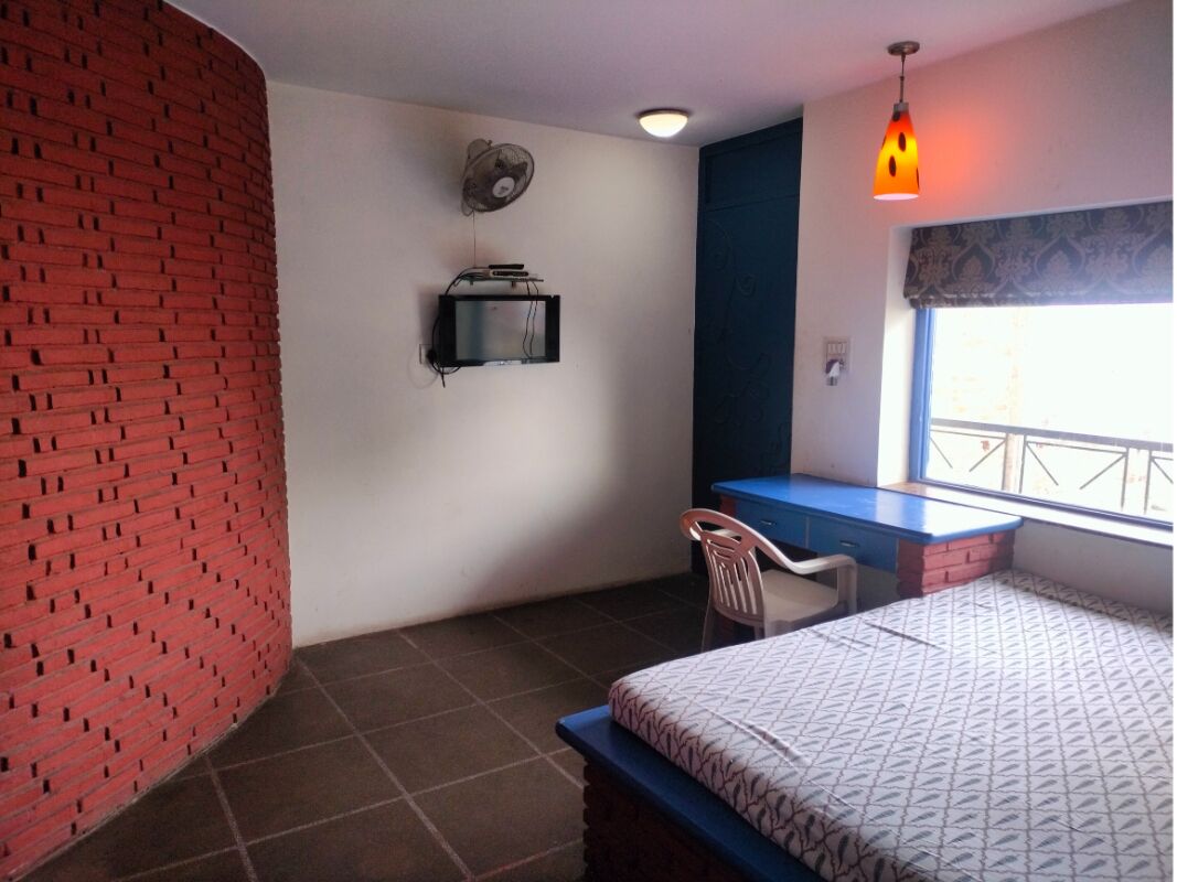 Une chambre avec un lit, un bureau, une chaise, un ventilateur et une fenêtre donnant sur un beau paysage.
