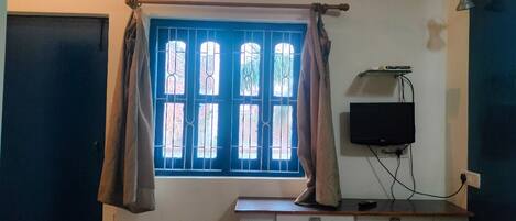 A room with a window, curtains, a television, and a desk.