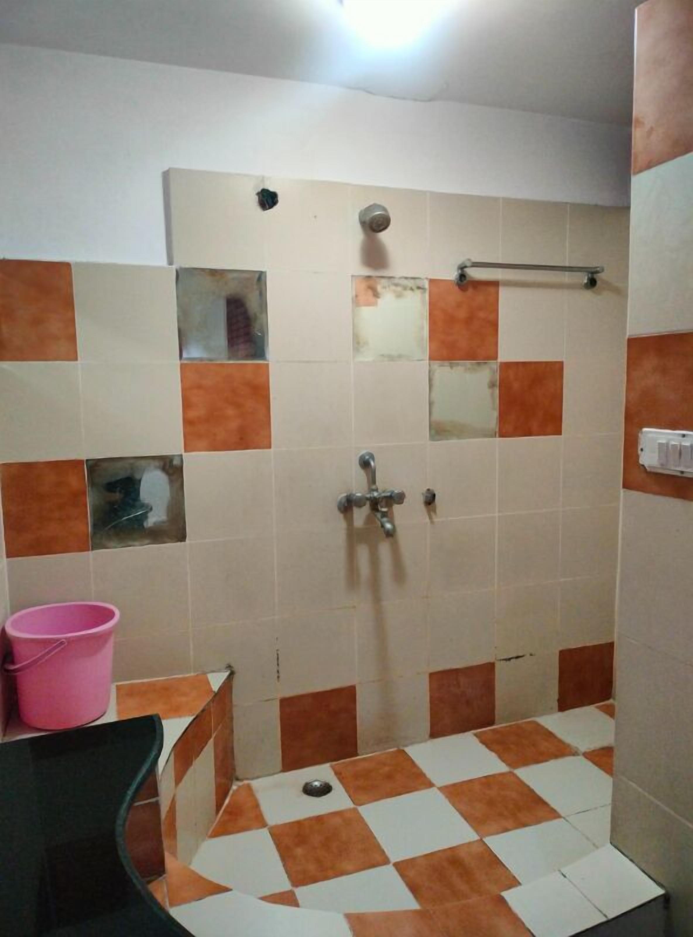 A bathroom with a shower, a sink, and a pink bucket.